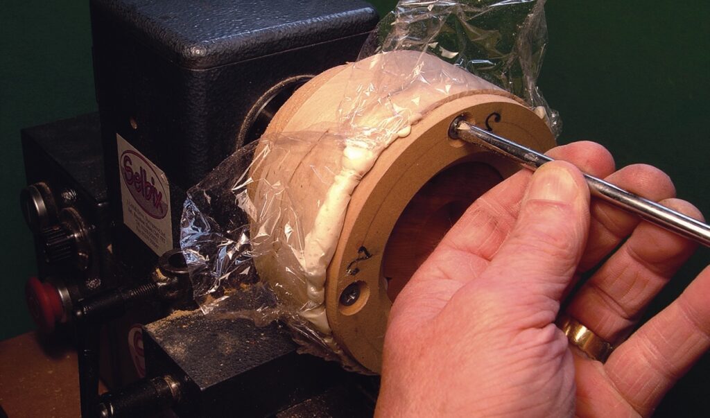 Hand securing object with screws on lathe.