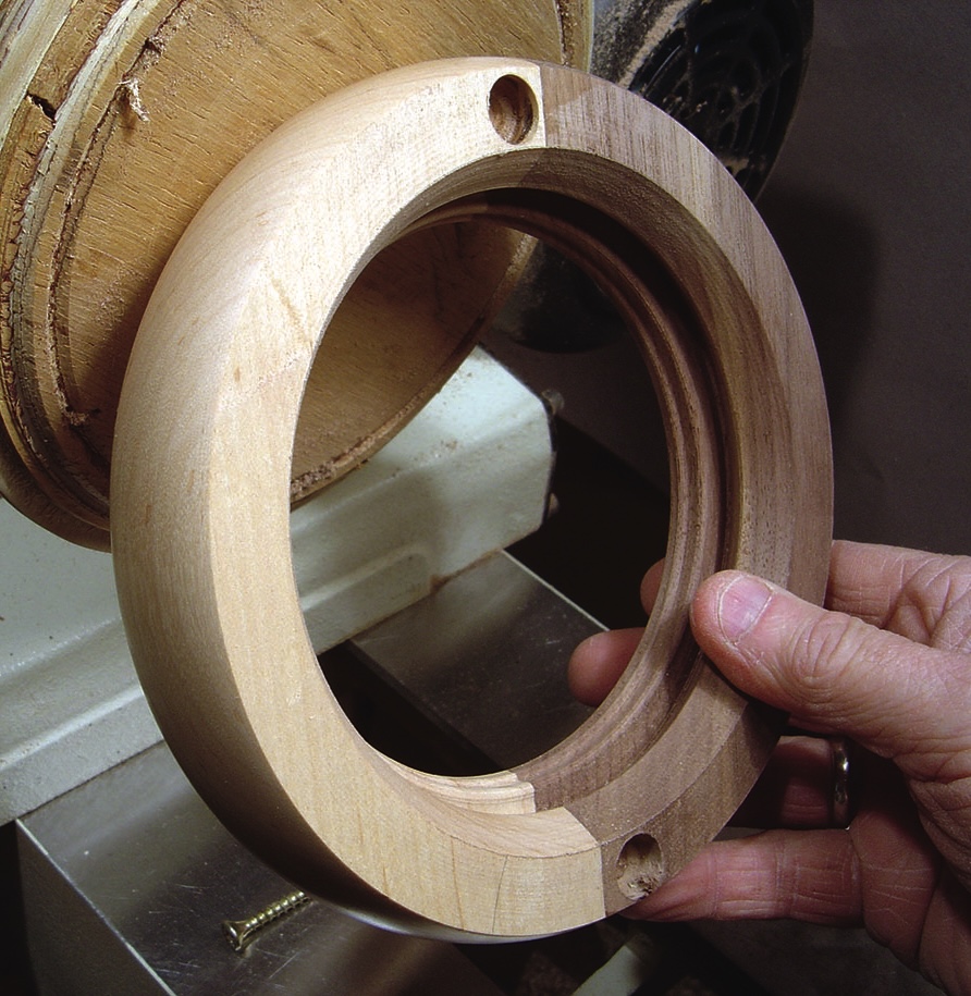Hand holding wooden circular frame on lathe.