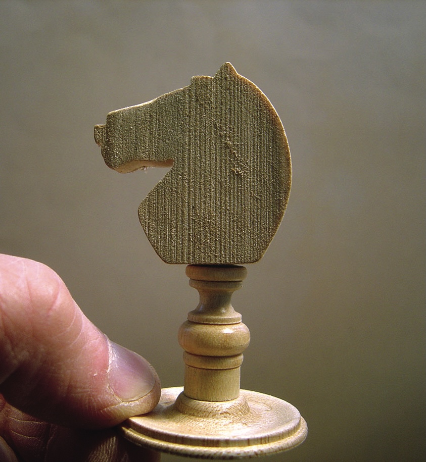 Hand holding wooden chess knight piece.