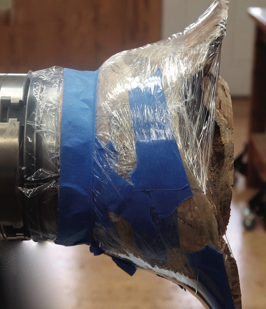 Wood wrapped in plastic and blue tape on lathe.