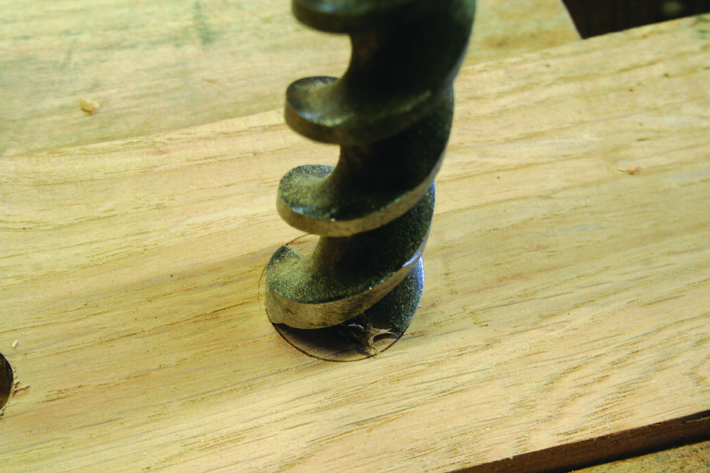 Drill bit creating hole in wooden plank.