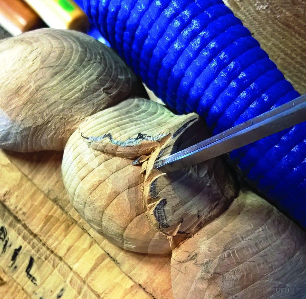 Wood carving with chisel and blue grip tool.