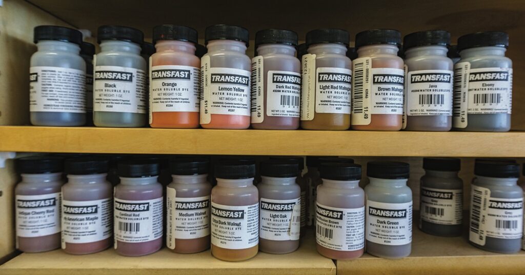 Assorted TransFast wood dye bottles on wooden shelves.