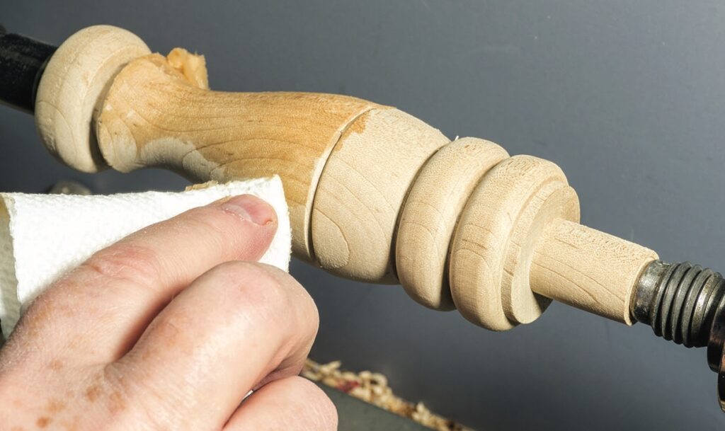 Sanding wooden spindle on a lathe