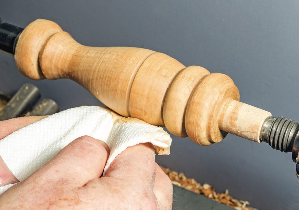 Craftsman polishing wooden spindle on lathe