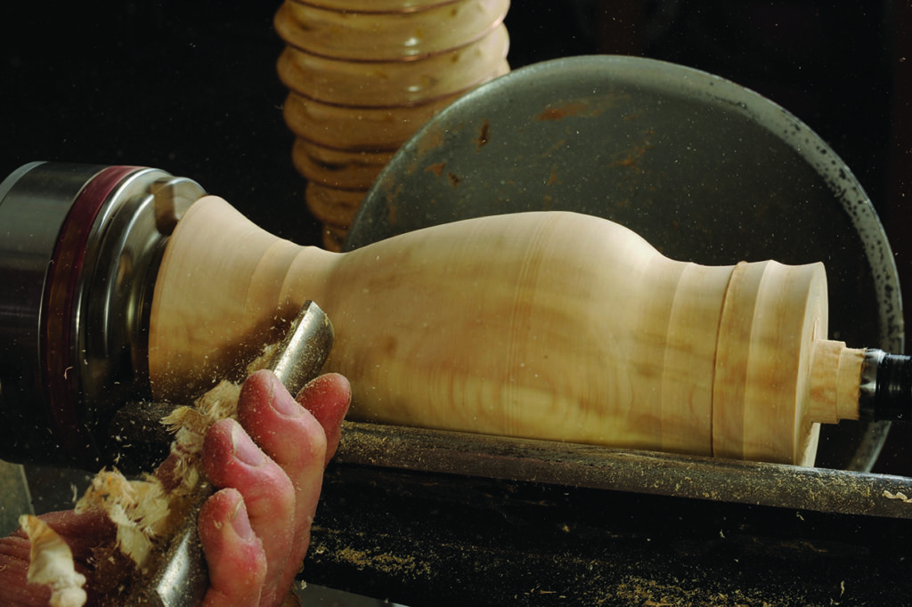 Woodturner shaping a wooden vase on a lathe