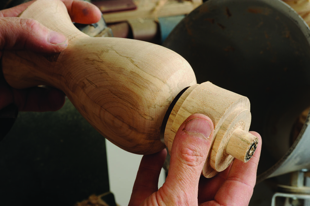 Hands shaping wooden object on a lathe.