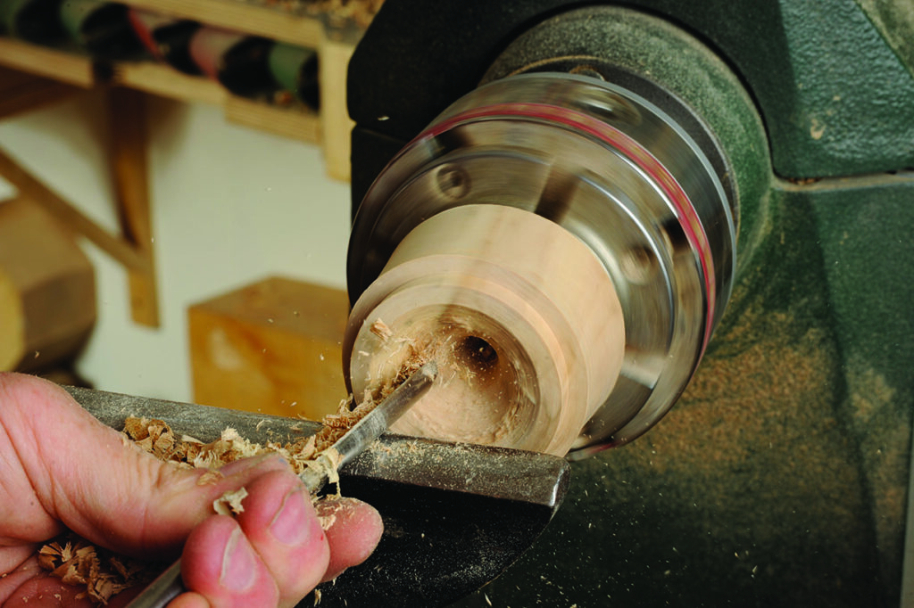 Woodturning on lathe, carving a wooden cylinder.
