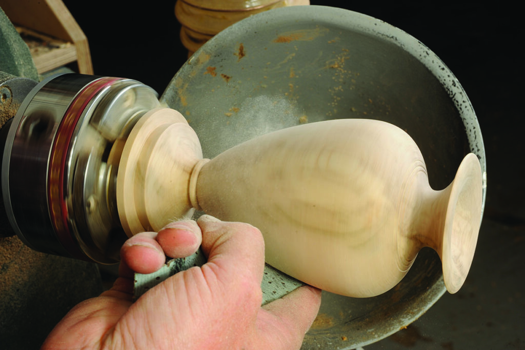 Craftsman using lathe to shape wooden vase.