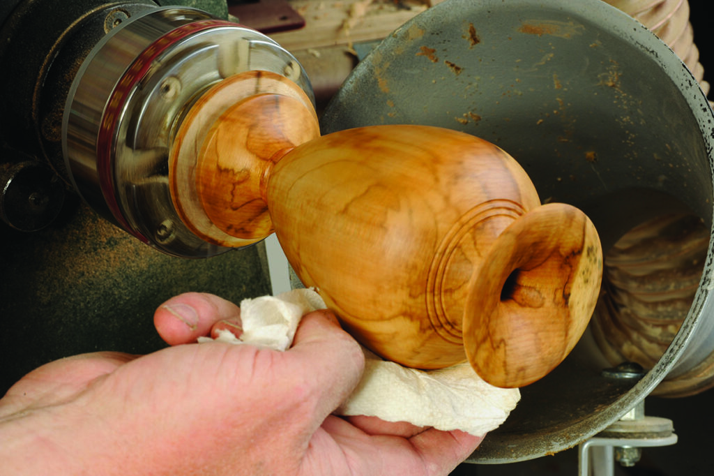 Craftsperson polishing wooden vase on lathe machine.