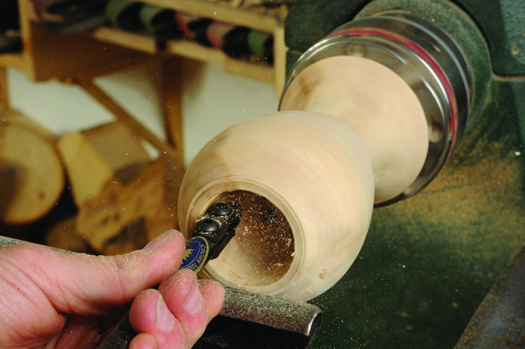 Woodturning tool shaping wooden bowl on lathe.