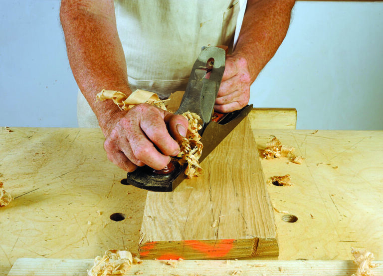Carpenter using hand plane on wooden board.