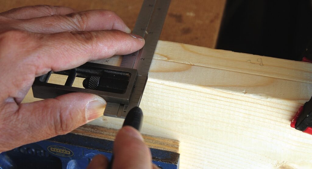 Measuring wood with a combination square and pencil.