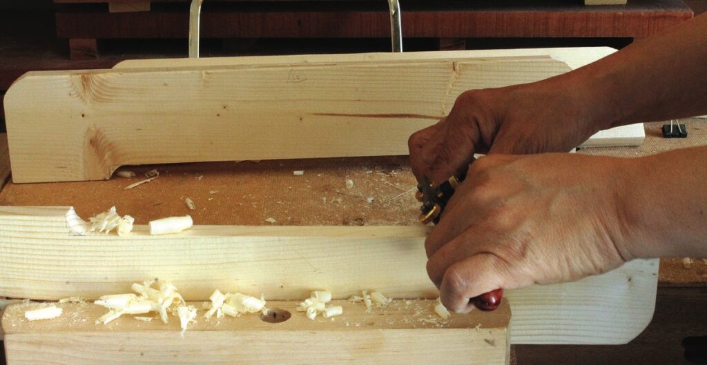 Person carving wood with hand plane tool.