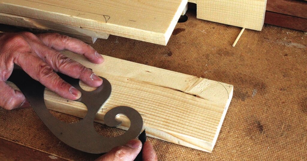 Hand tracing pattern on wooden planks with stencil.