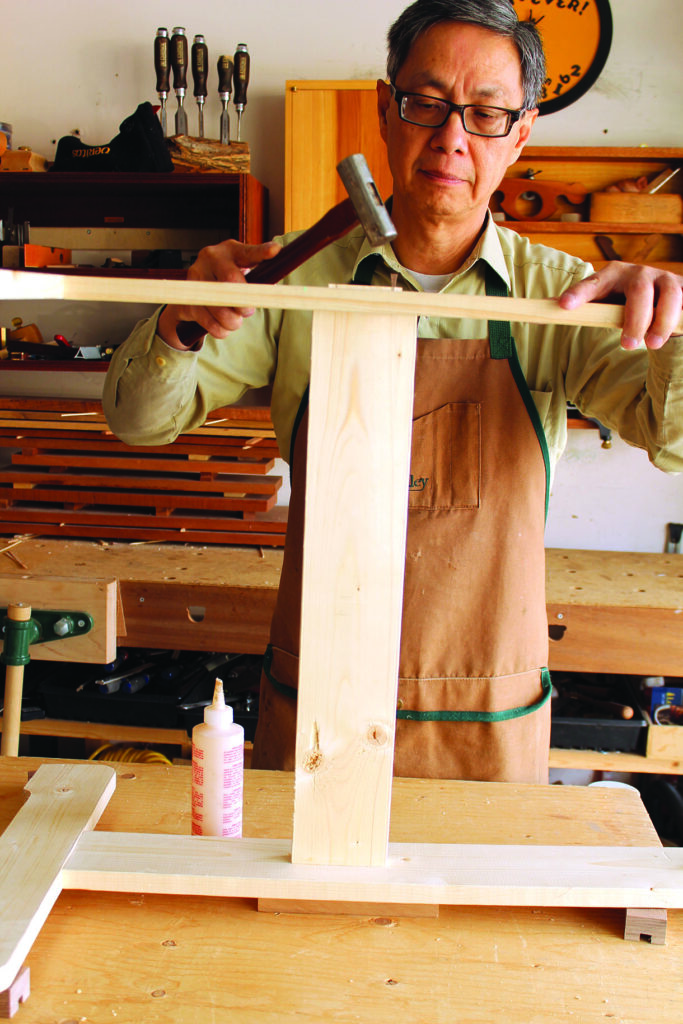 Person hammering wood pieces in a workshop.
