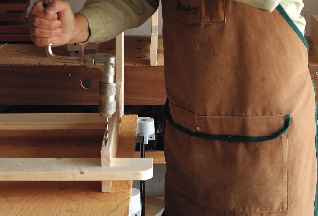 Woodworker using brace and bit on wood frame.