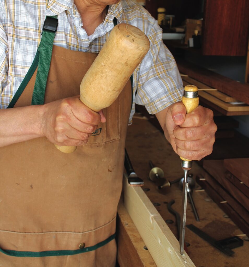 Craftsman chiselling wood in workshop.