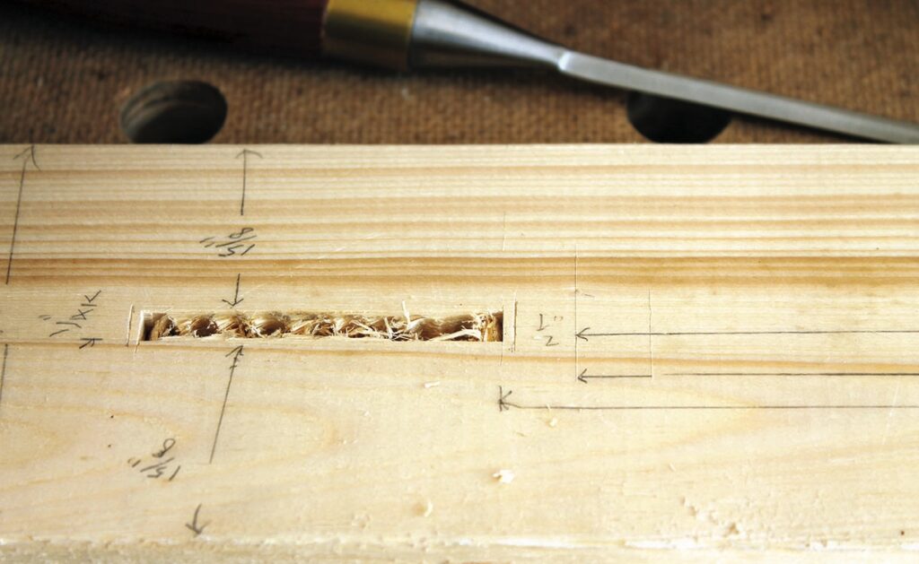 Wood mortise joint with chisel on wooden surface.