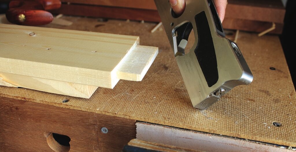 Craftsman using plane on wooden boards.