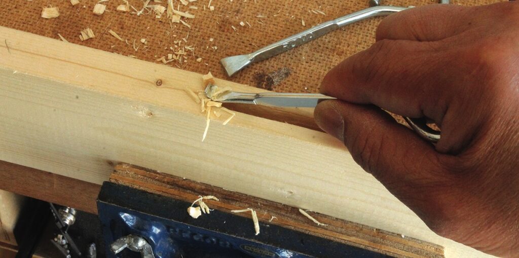 Hand carving wood with a chisel and vise.