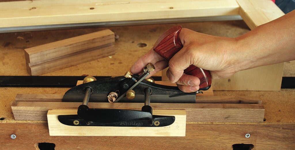 Hand using a wood plane on wooden surface.