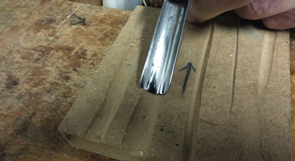 Carving wood with metal tool on workbench.