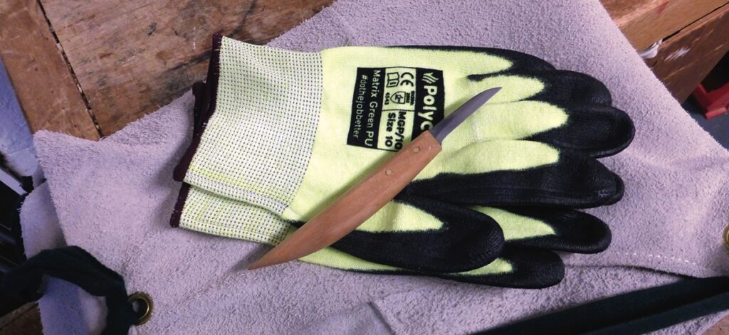 Safety gloves and knife on wooden table.