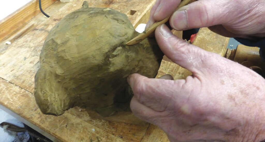 Person sculpting clay with wooden tools.