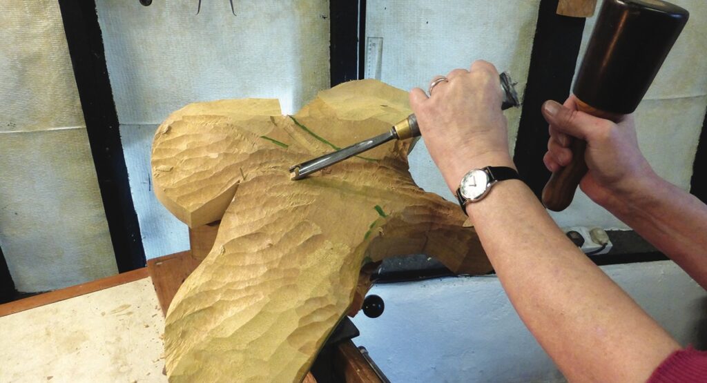 Person carving wood with chisel and mallet.