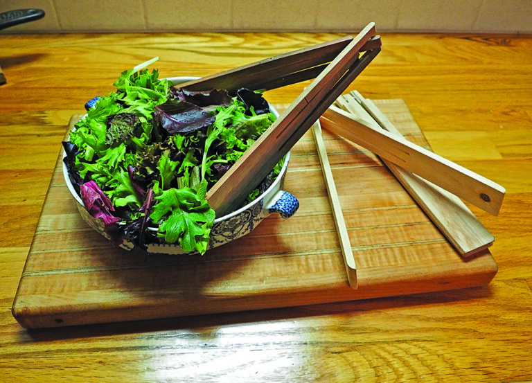 Bowl of leafy salad on wooden board.