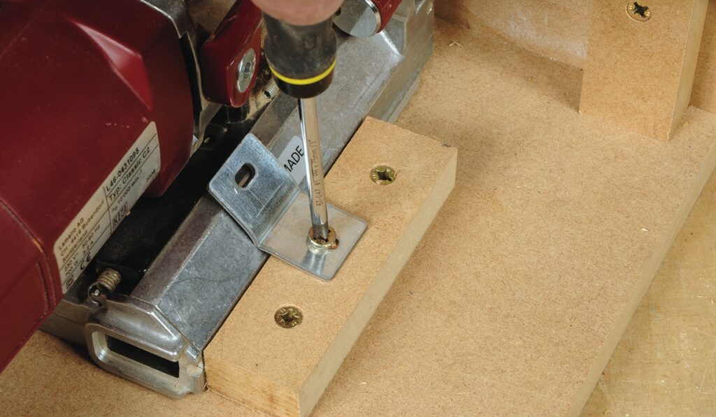 Screwdriver securing metal bracket on wooden surface.