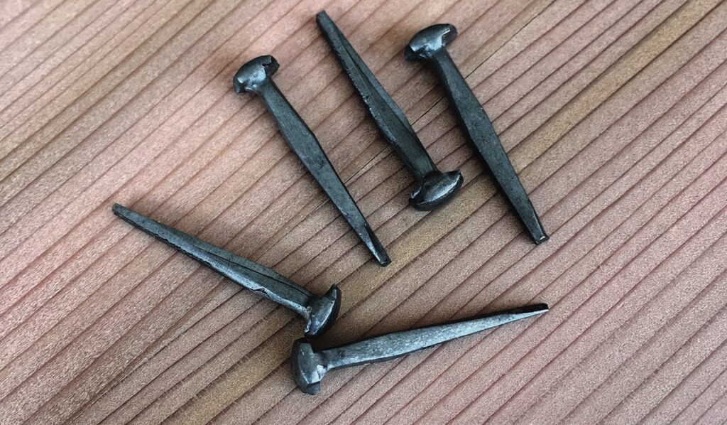 Five wrought iron nails on wooden surface.