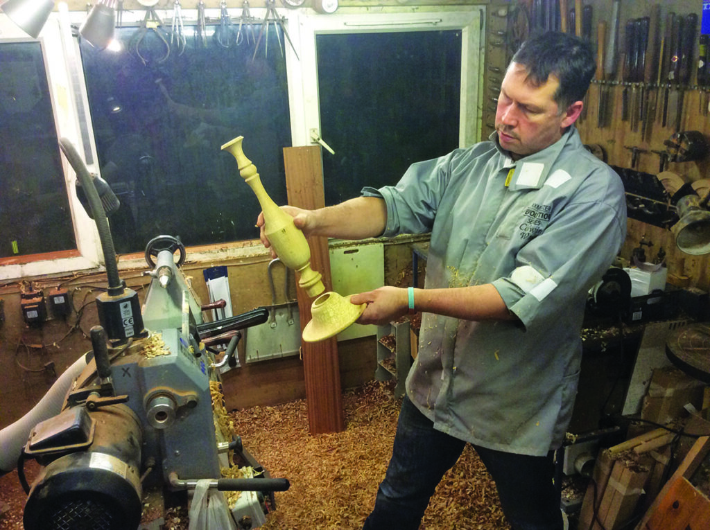 Man inspecting wooden candlestick in workshop.