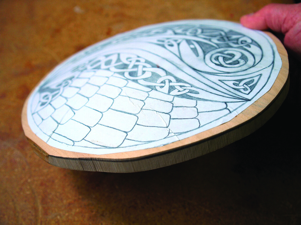 Person holding wood with Celtic design sketch.