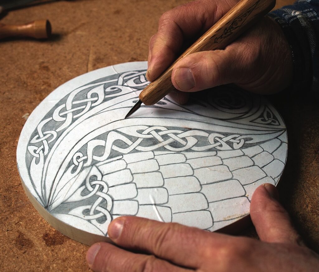 Hand carving intricate design on round wood piece.