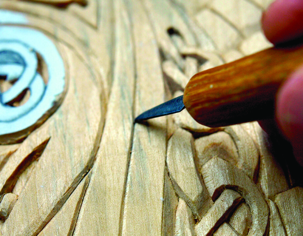 Wood carving with intricate design and carving tool.
