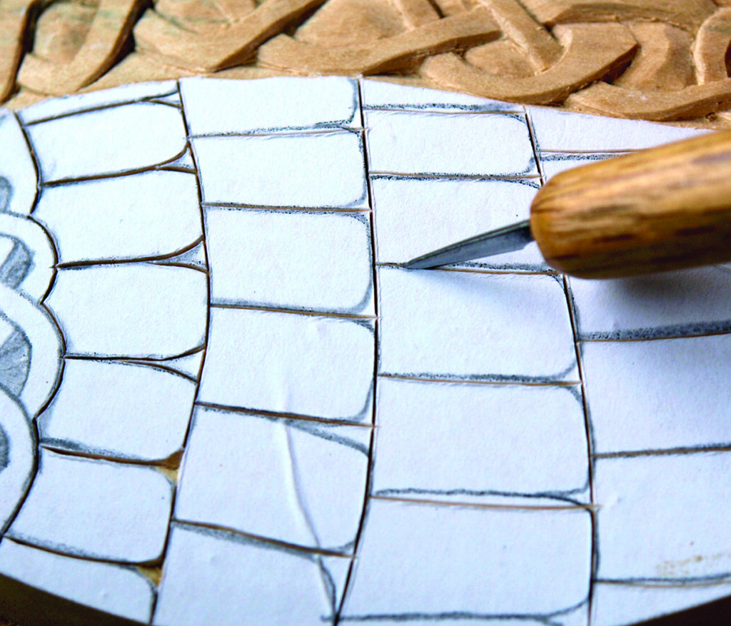 Wood carving design with chisel on paper template.