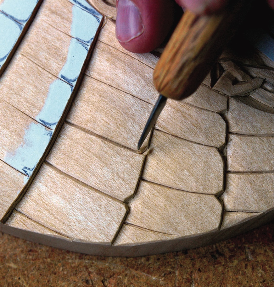 Hand carving intricate wood design with chisel.