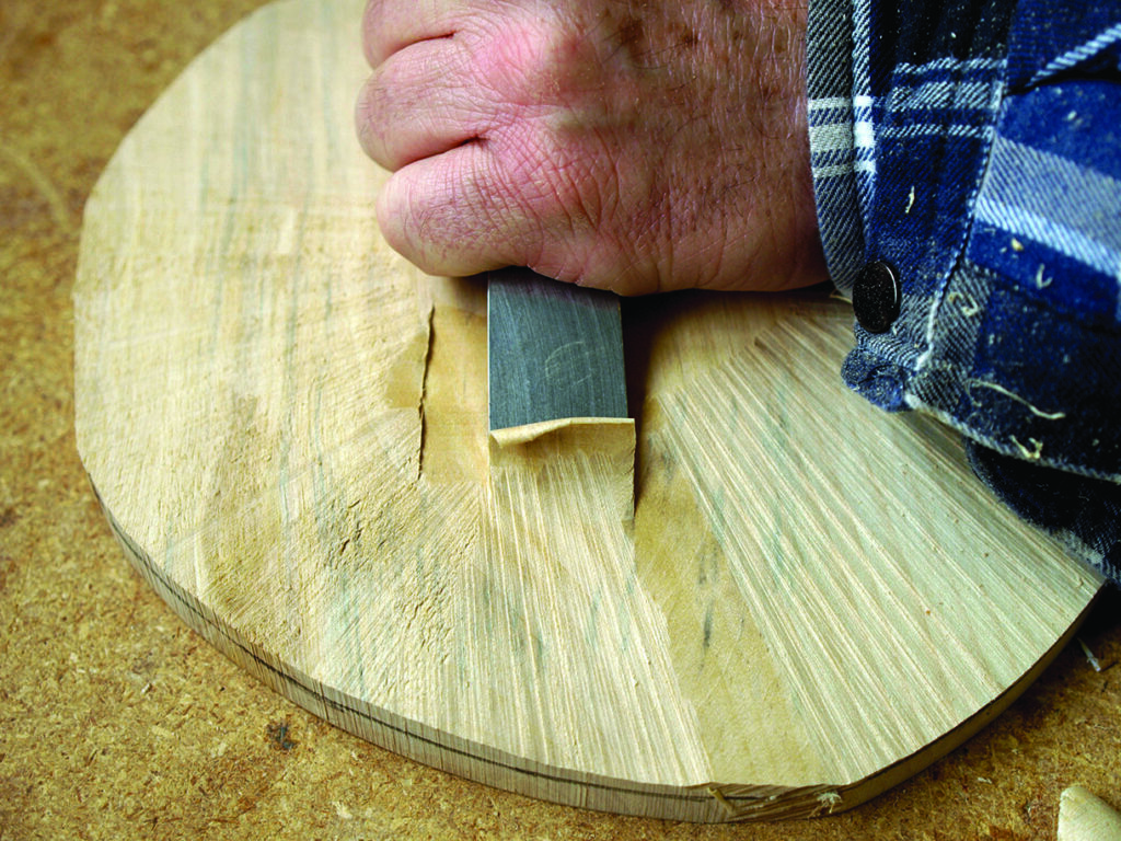 Woodworker carving round wood piece by hand