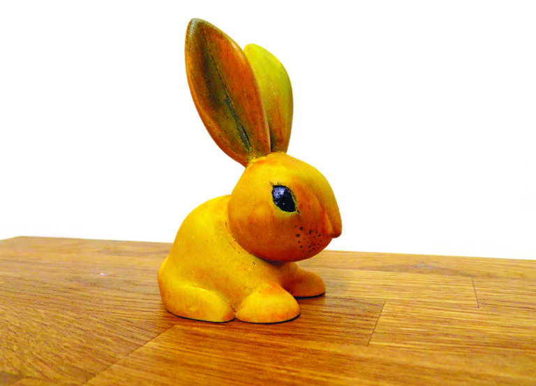Yellow ceramic rabbit on wooden table.