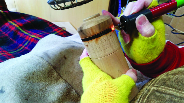 Person woodburning a design on wooden item.