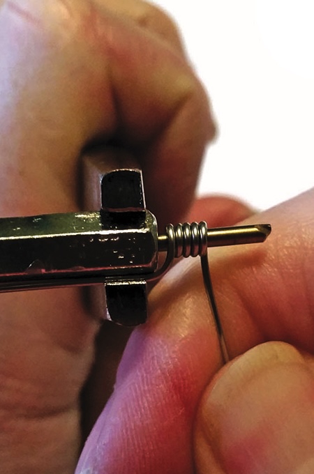 Hand using pliers to wrap wire coil.