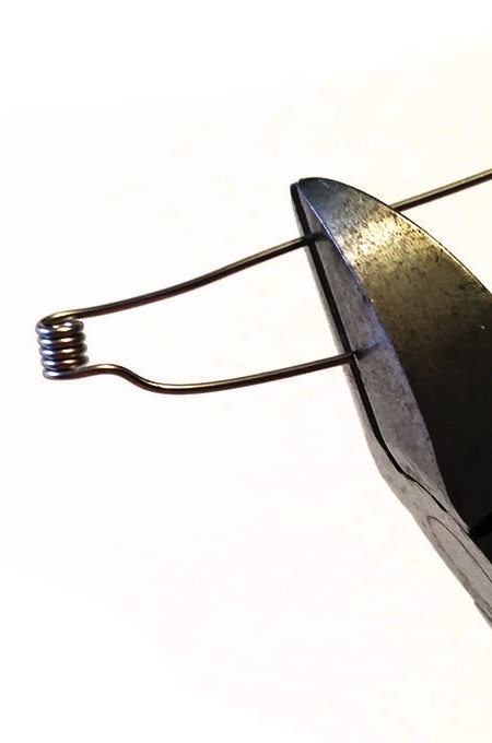 Pliers twisting metal wire end into spring shape.