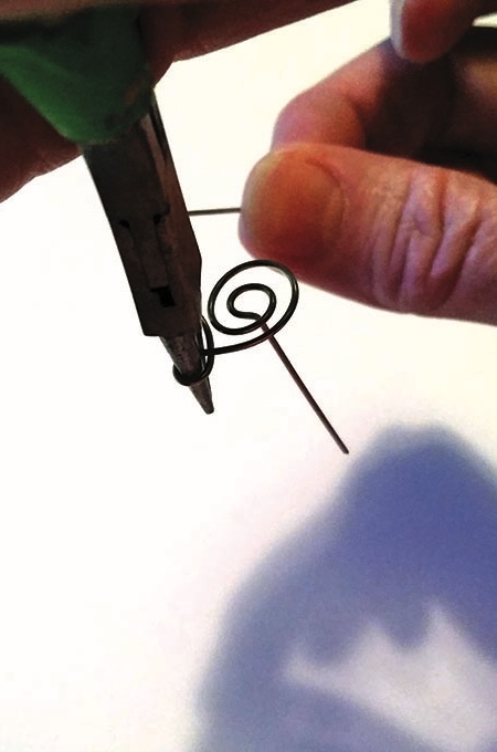 Hands using pliers to twist wire spiral