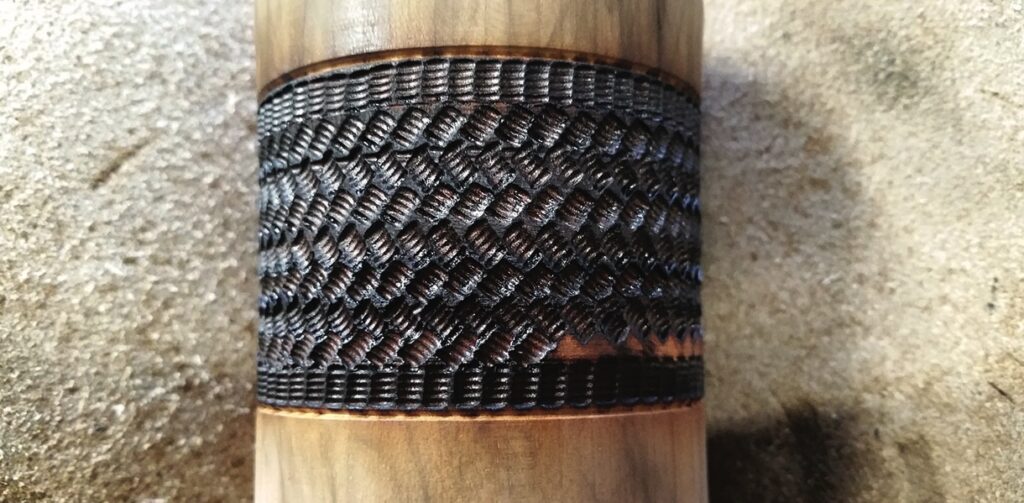 Wooden staff handle with black decorative pattern.
