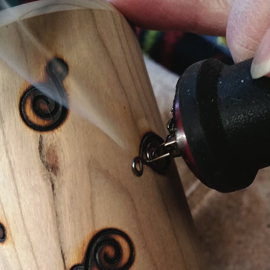 Wood burning tool creating spiral design on wood.