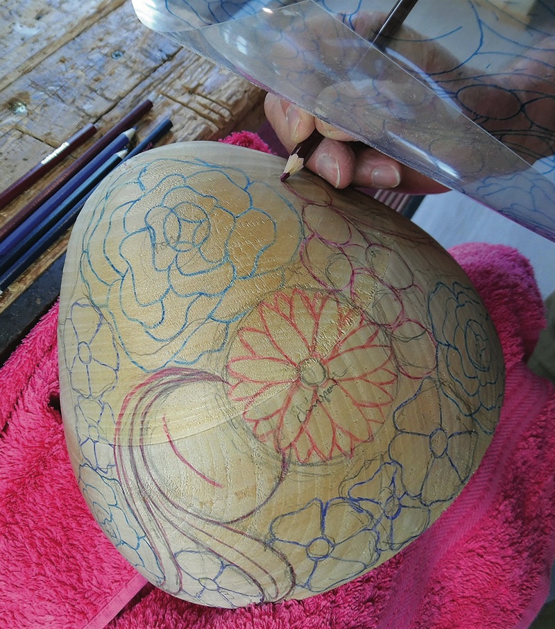 Person drawing floral designs on a wooden bowl.