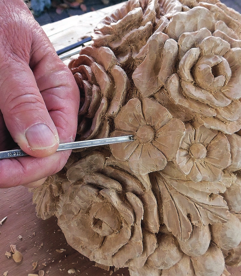 Wood carving of floral design being crafted by hand.