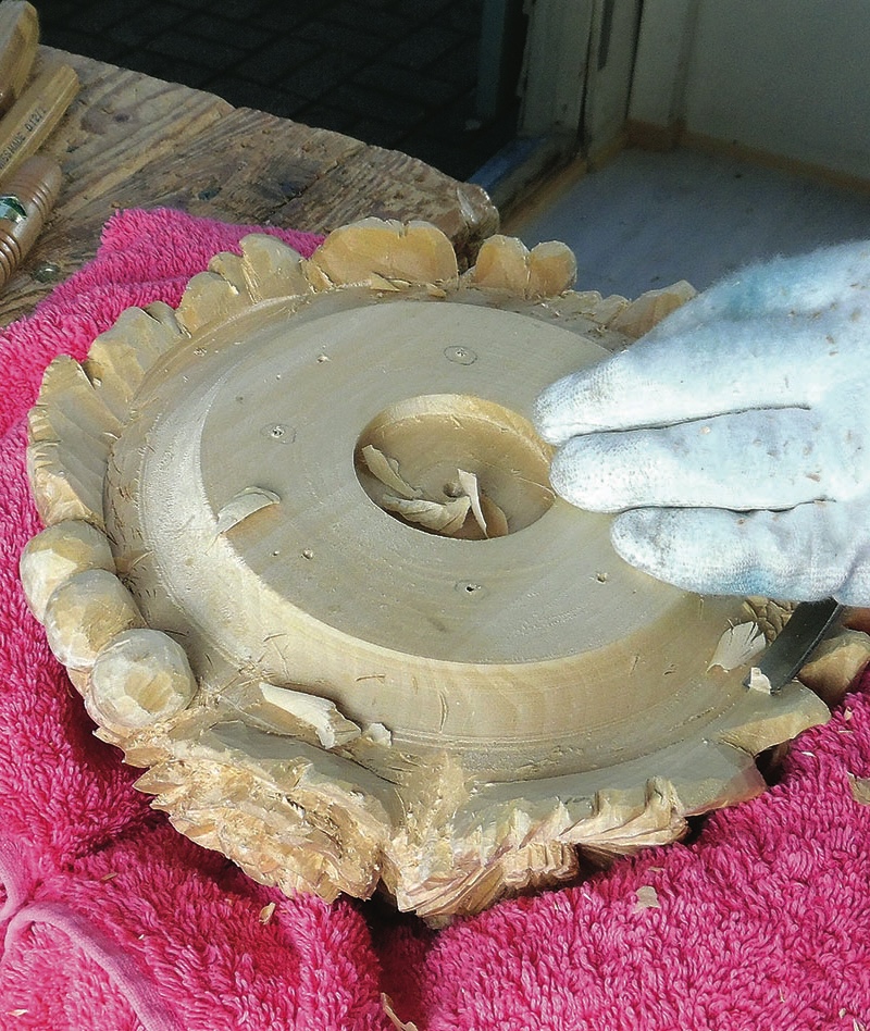 Hand carving circular wooden piece on pink cloth.